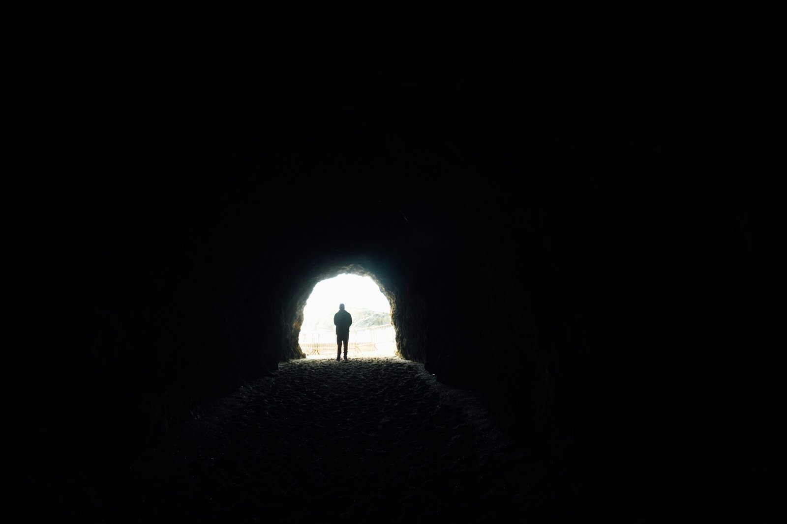 Person navigating a dark transition tunnel toward a distant light.